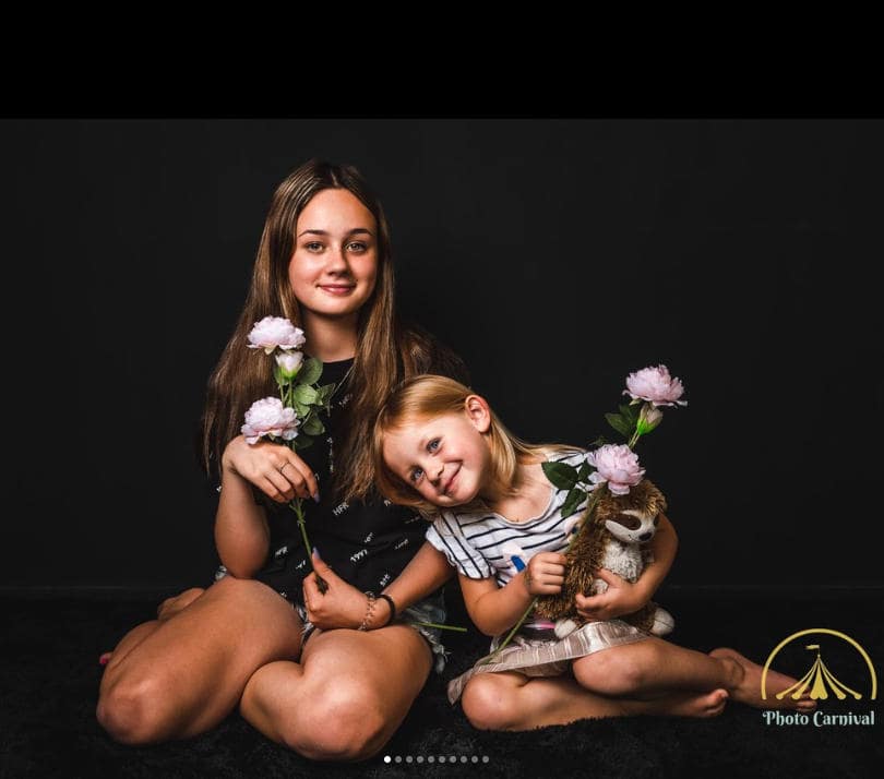 Two girls smiling with flowers and stuffed toy.