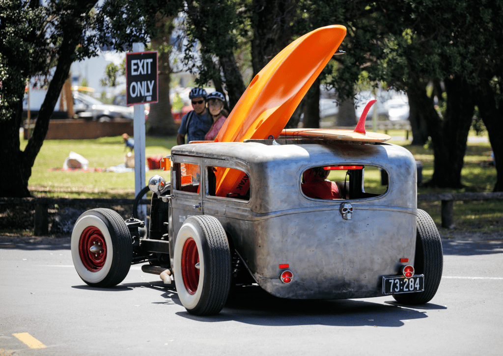 Vintage hot rod with orange surfboard at outdoor event.